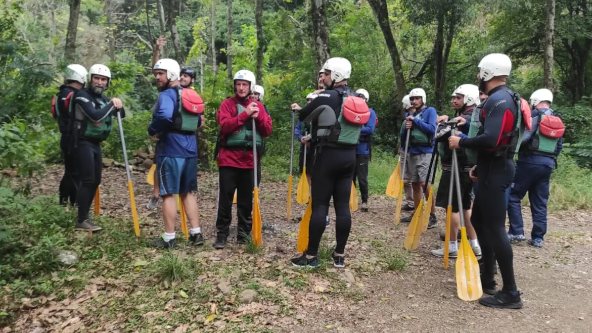 pessoas com roupas especiais e equipamentos para prática de rafting em pé, na trilha, recebendo orientações.